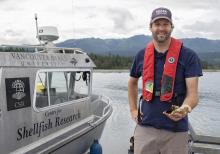 Dr. Timothy Green, VIU’s Canada Research Chair in Shellfish Health and Genomics stands on a dock next to a boat holding oysters in his hand.