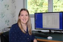 VIU Psychology Professor Becky Earhart sitting at her desk in front of a computer screen and smiling at the camera.