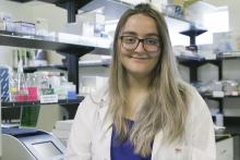 Kimberley Barrett wears a white lab coat and stands in a research lab.