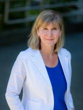 Kristie Dewald with a blurred background, wearing a white blazer