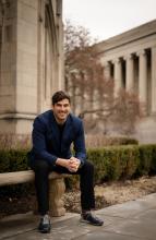 Michael MacKenzie sits on a bench in front of a stone building