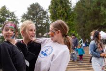 Three young girls wearing face paint hug, with a crowd on the stairs behind them