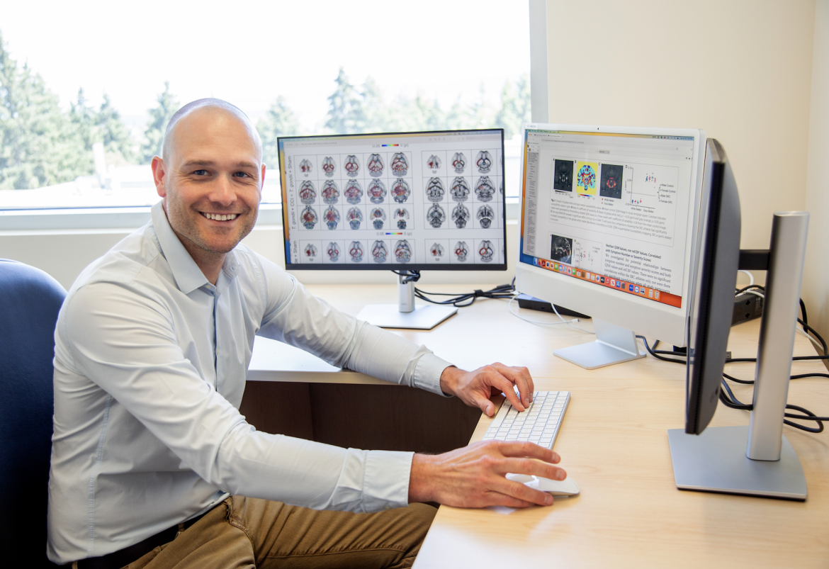 Dr. Sandy Shultz sitting at a desk in front of two computer screens and smiling at the camera.